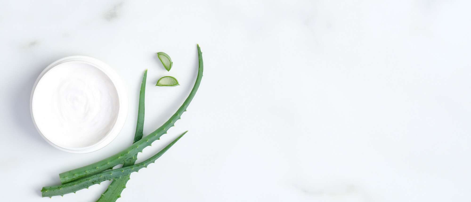 Natural Cosmetic Skincare Moisturizer Cream Jar And Sliced Stems Aloe Vera On Marble Background. Flat Lay, Top View. Skin Care And Beauty Treatment Concept.